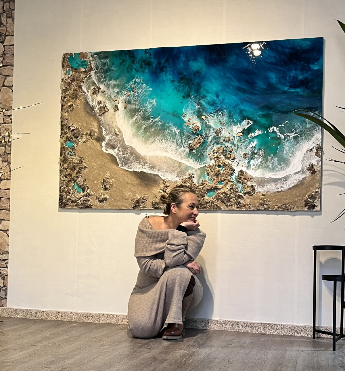 Eva Jurado sentada delante de una obra de playa en resina de gran formato colgada en la pared