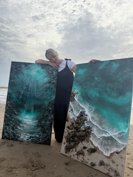Eva Jurado en la playa, sujetando dos obras verticales de Ocean Art