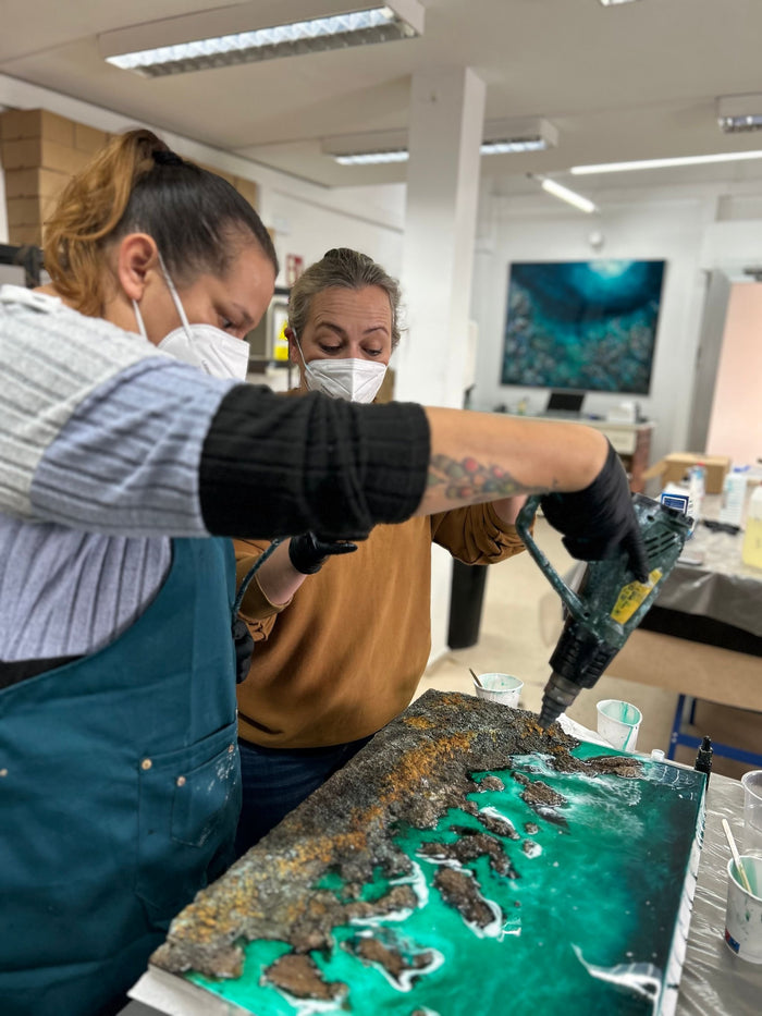Alumnas trabajando la resina con soplete sobre una obra turquesa