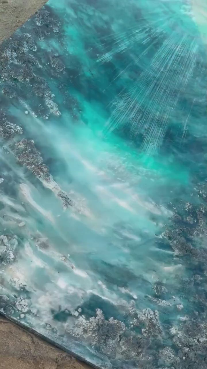 Eva Jurado sujeta en la playa una obra de Ocean Art turquesa con rayos de luz